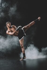 side view of concentrated muay thai fighter practicing kick isolated on black, fight club concept